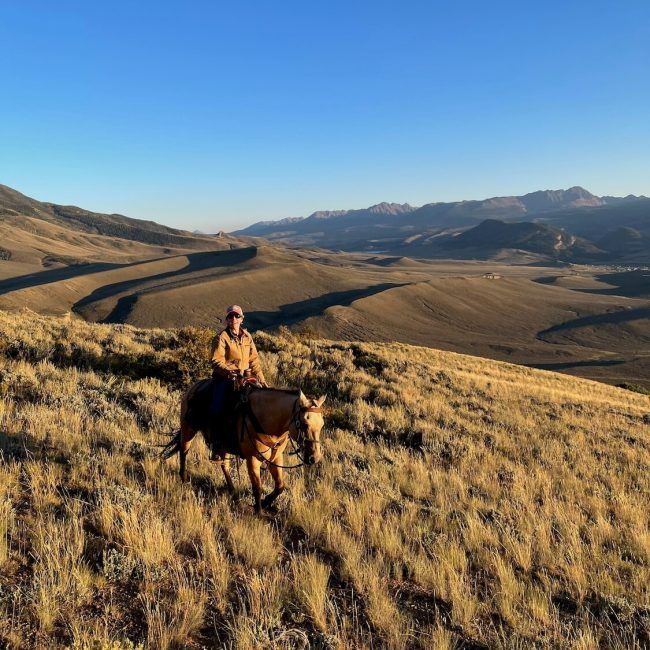 Western rider on horseback following a scenic ranch trail surrounded by Colorado mountain views at Rusty Spurr Ranch.