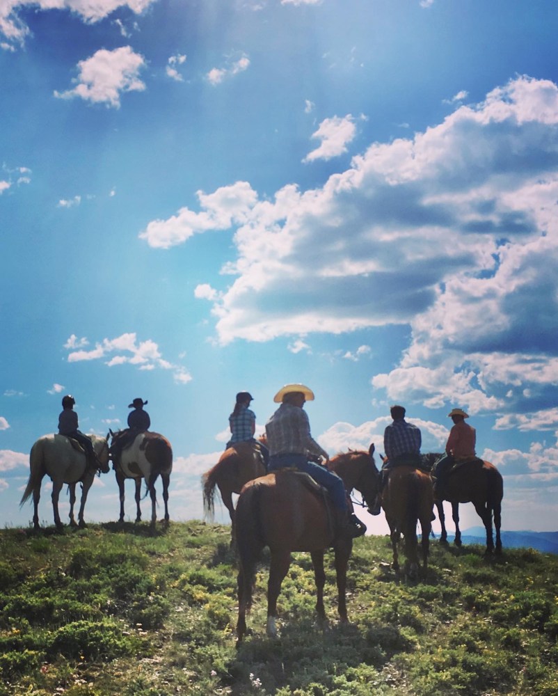 Riders on horseback exploring scenic Colorado wilderness at Rusty Spurr Ranch, showcasing the expansive views from the top of a mountain.