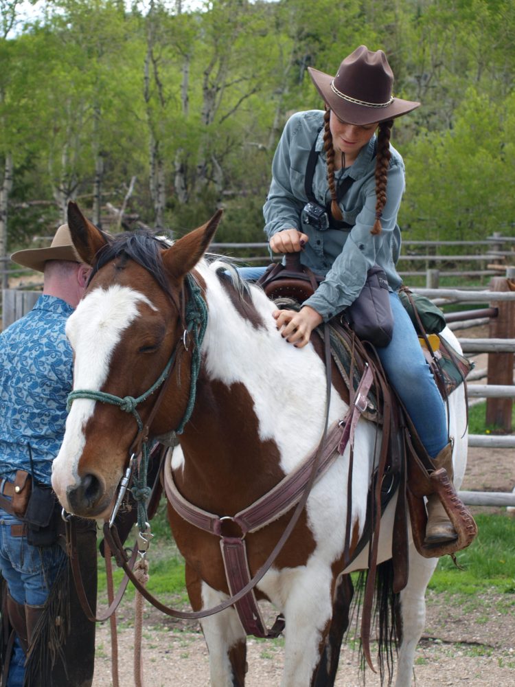 A wrangler adjusts the saddle for a rider before setting out on a horseback trail ride, emphasizing the safety and well-being of the guests and horses.