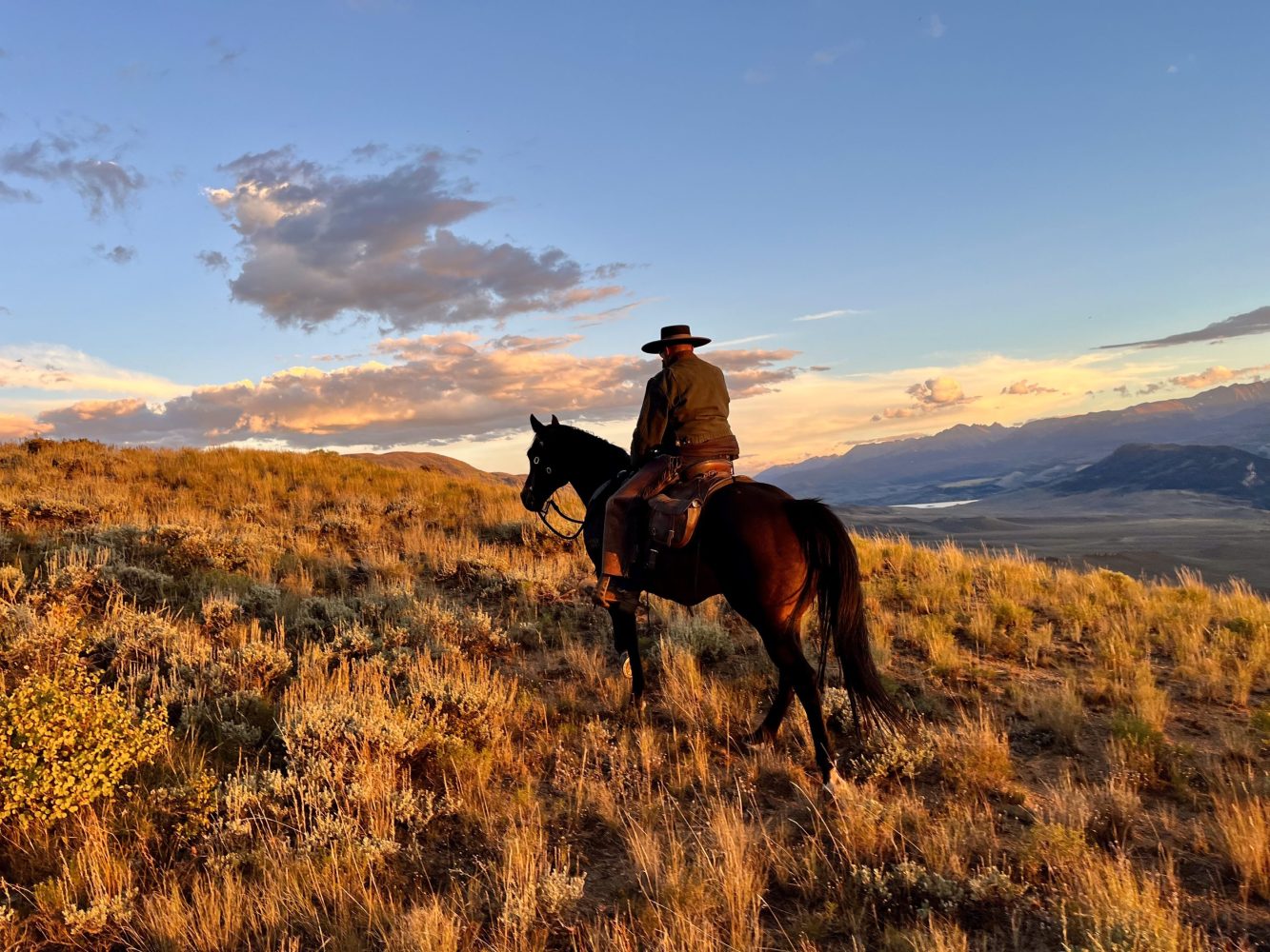 A rider on horseback traversing a trail at the Rusty Spurr Ranch with the majestic Rocky Mountains in the background.