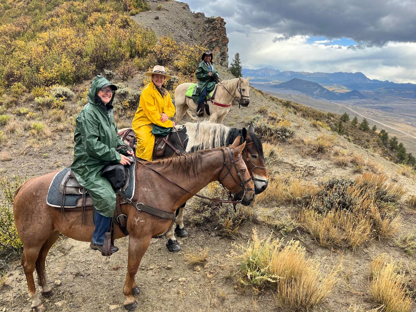 Riders wearing raincoats and riding horses in the rain at Rusty Spurr Ranch